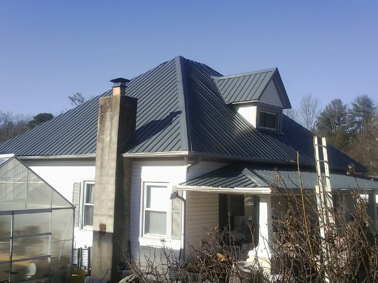 Dark blue standing seam metal roof on a white farmhouse with dormer — Slate & Tile Roof Repair by Roofing Brothers in Ganado