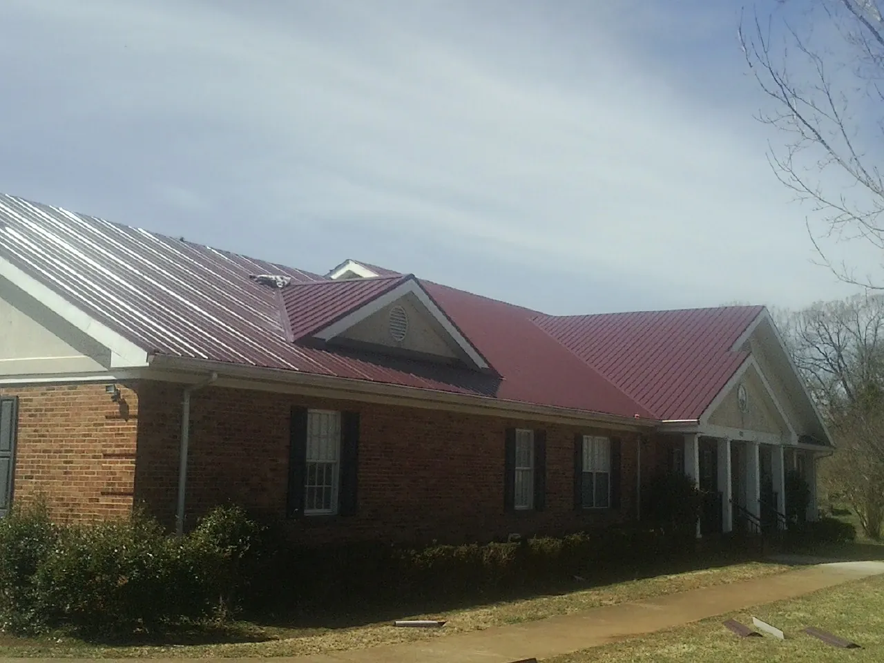 Red metal roof with gabled entries on a long brick building, from a Hail Damage Roof Repair job in Ganado