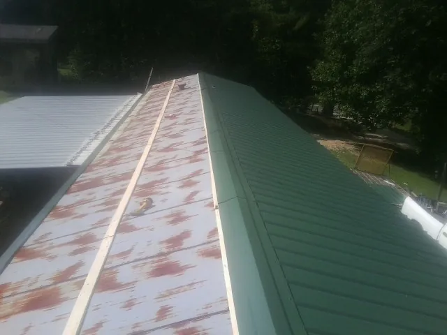 Old rusted panels beside newly installed green metal roofing — Wind Damage Roof Repair by Roofing Brothers in Ganado
