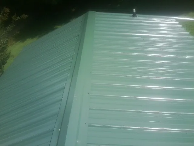 New green metal panels meeting at the ridge of a roof — Flat Roof Repair work by our crew in Ganado