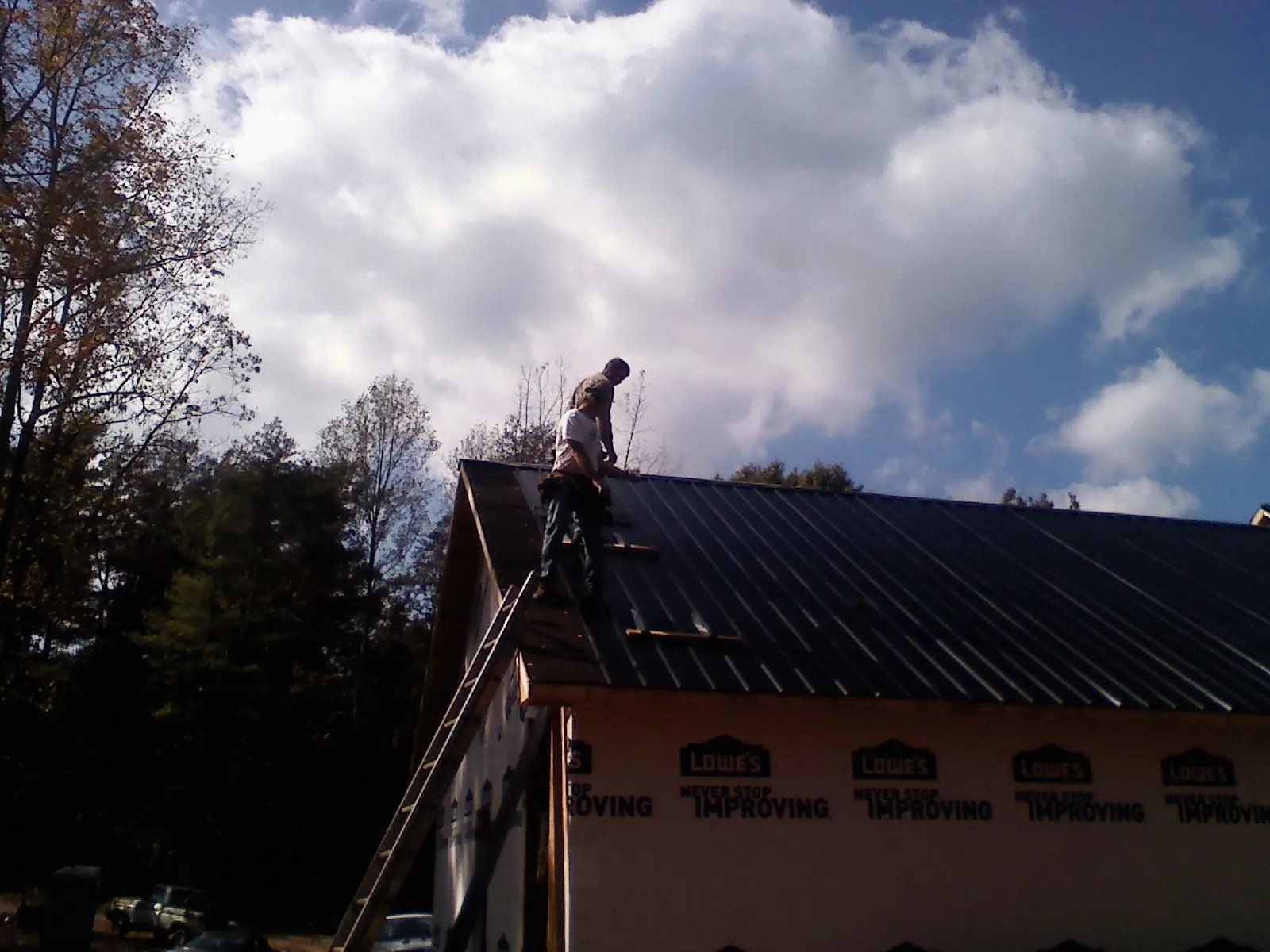Roofer fastening dark metal panels high against a cloudy sky, from a Roof Inspection job in Ganado