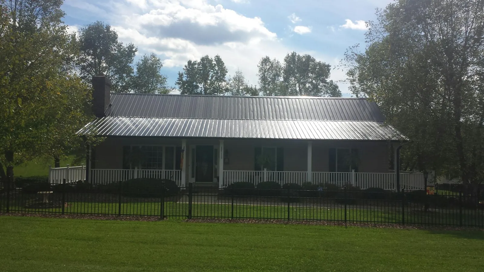 Gray metal roof on a brick ranch with a full width front porch — Gutter Guard Installation work by our crew in Ganado