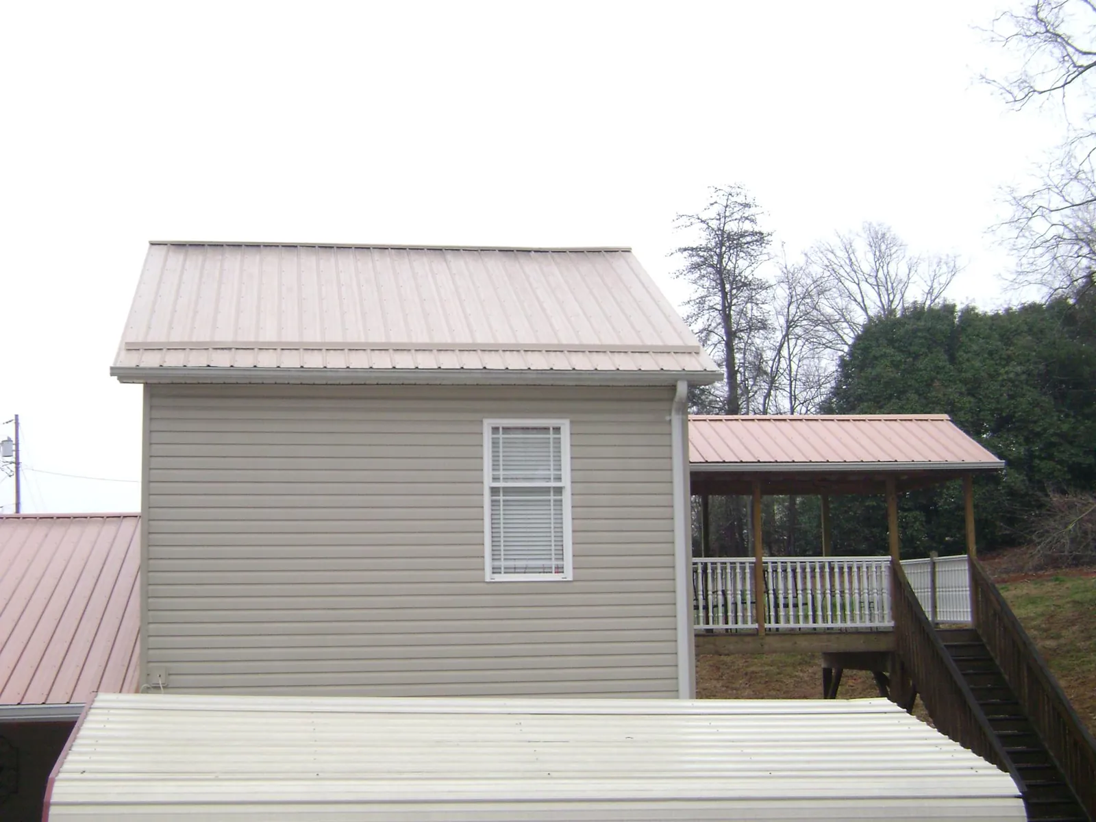 Tan metal roofs on a two story addition and attached porch, from a Roof Replacement job in Ganado